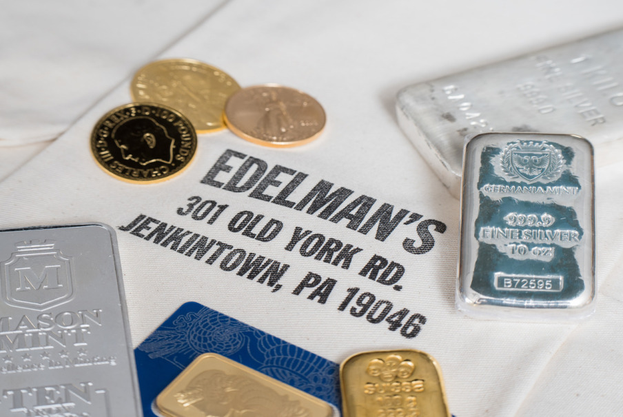 Gold and silver bullion bars and gold coins displayed on a cloth with Edelman’s business name and address