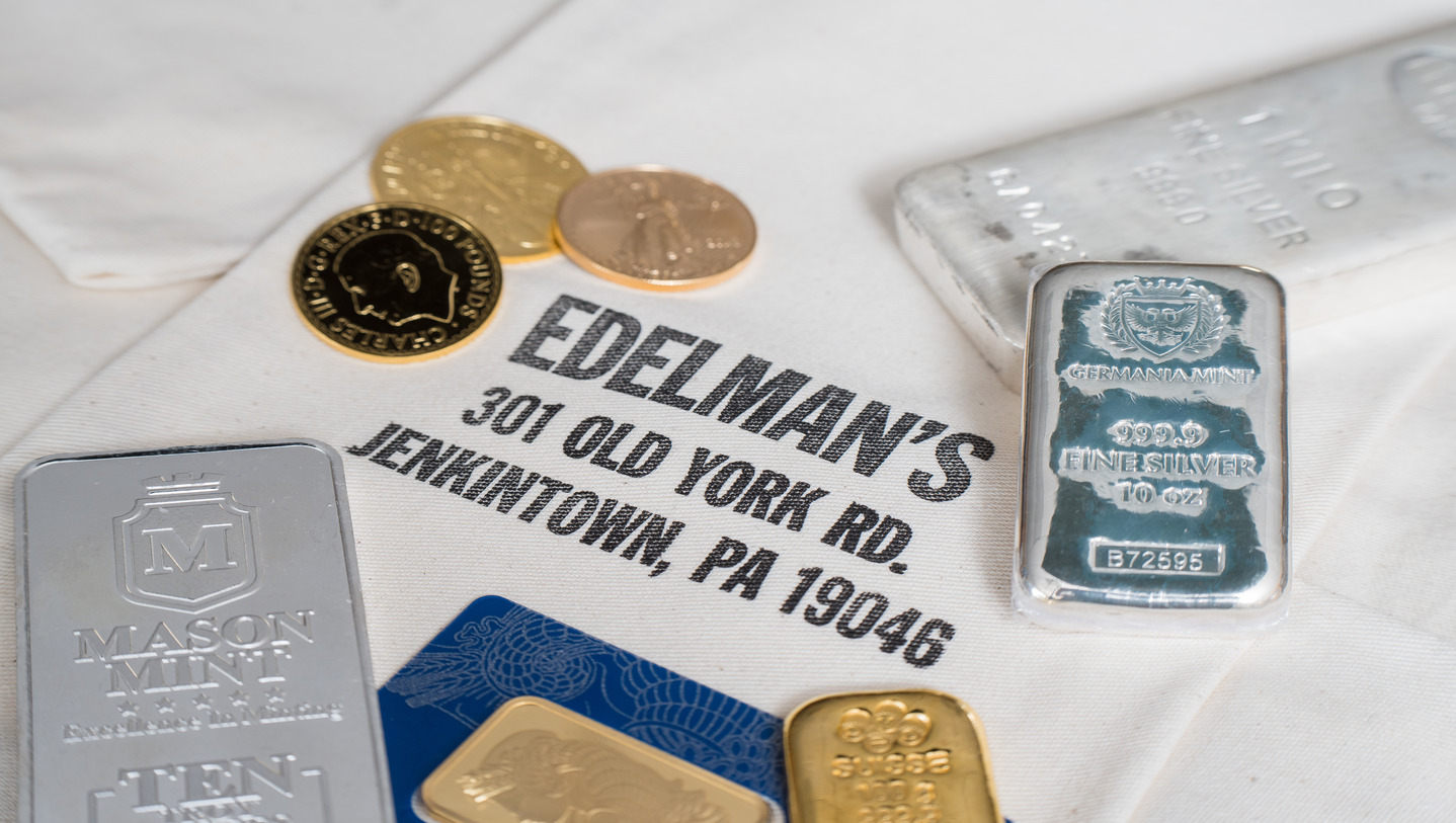 Gold and silver bullion bars and gold coins displayed on a cloth with Edelman’s business name and address